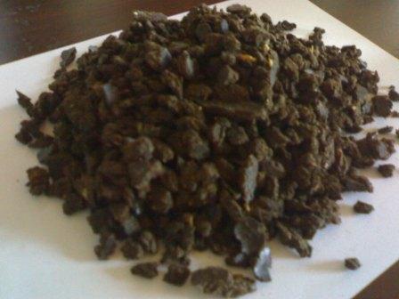 Kupa ciemnego pelletu z łuski słonecznika na białym tle, widoczne drobne, jaśniejsze fragmenty łuski.